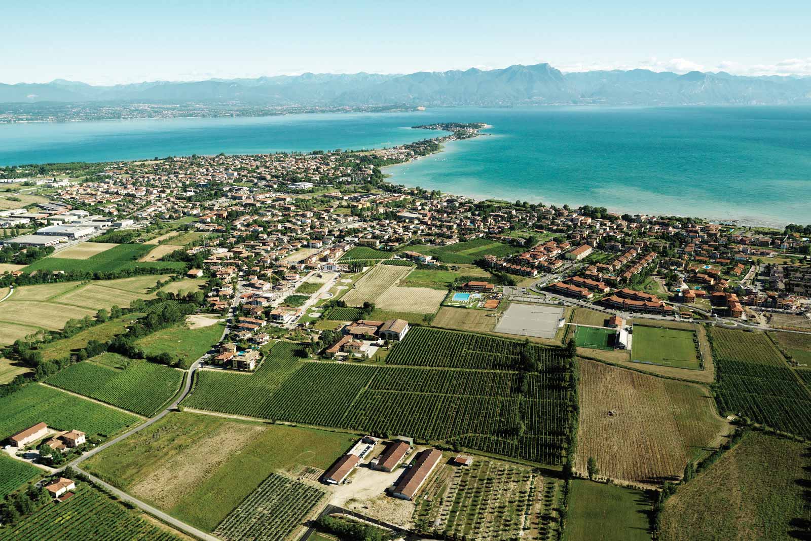 An aerial view of Lugana DOC reveals its proximity to Lake Garda and the Alps in the distance. ©Consorzio Tutela Lugana DOC